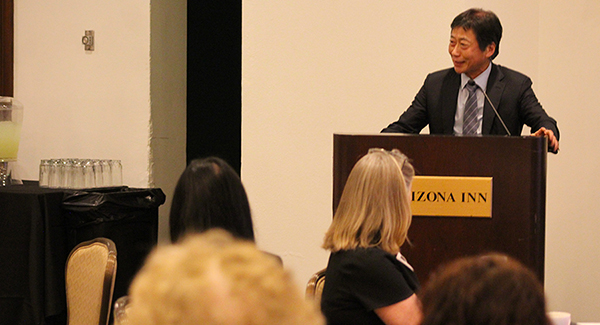 [Asian man with suit and tie at podium smiles to audience as he comments on recent faculty promotions in the Department of Medicine at the U of A College of Medicine – Tucson.]