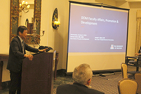 [Asian man in suit-and-tie at podium in front of ornate mirror and a blue screen that says, “DOM Faculty Affairs, Promotion & Development,” with a University of Arizona logo in the bottom right corner]