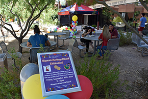 [Flyer for the Hispanic Heritage Month Celebration displayed with balloons at event hosted by UAHS Office of Equity, Diversity & Inclusion in Hippocrates Courtyard between the U of A College of Medicine – Tucson and the R. Ken Coit College of Pharmacy]