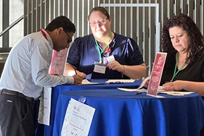 [Nephrology administrative assistant Gina Favela (right) and a colleague ready to greet and assist someone in signing in for the Tucson Transplant Symposium in the lobby of the Health Sciences Innovation Building.]