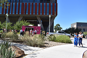 [With the Health Sciences Innovation Building behind them, people gathering for the Hispanic Heritage Month Celebration line up at the Ensenada Street Food truck for meat and vegetarian tacos and burritos.]