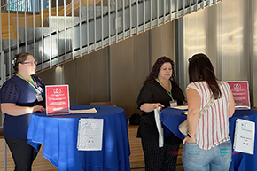 [Nephrology administrative assistant Gina Favela (center) and a colleague ready to greet and assist someone in signing in for the Tucson Transplant Symposium in the lobby of the Health Sciences Innovation Building. ]