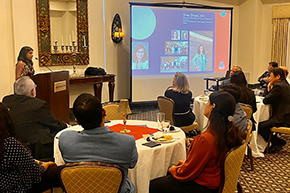 [Woman at podium with people watching her seated at round tables to her front, and a screen displaying slide with name and photos of Sima Ehsani, MD]