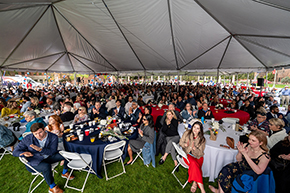 [Families, friends and faculty of medical students, including Drs. Sairam Parthasarathy and Indu Partha – front and center, gather under a tent erected this year due to stormy weather forecast for March 15, 2024, in Tucson. (Photo courtesy UArizona Health Sciences)]