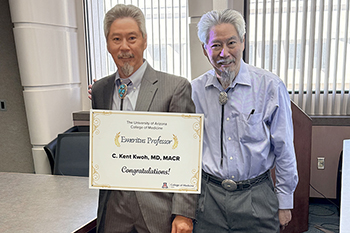 [Image of University of Arizona Arthritis Center director and retired chief of the Division of Rheumatology C. Kent Kwoh, MD, MASC, next to life-size cutout poster of himself with sign that says, “Emeritus Professor C. Kent Kwoh, MD, MACR – Congratulations!” with the U of A College of Medicine – Tucson logo.]