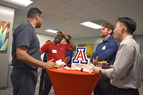 [Residents and med students, including Ethan Ross and Nhat Nguyen (right), rub elbows at the Internal Medicine Student Meet-and-Greet at the College of Medicine – Tucson social hall.]