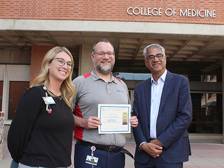 [Beth Draves, RN, senior director and associate CNO for Banner hospitals in Tucson, presents Josh Malo, MD, with his Good Catch Patient Safety Award, with Sai Parthasarathy, MD, chief, Pulmonary division chief, looking on.]