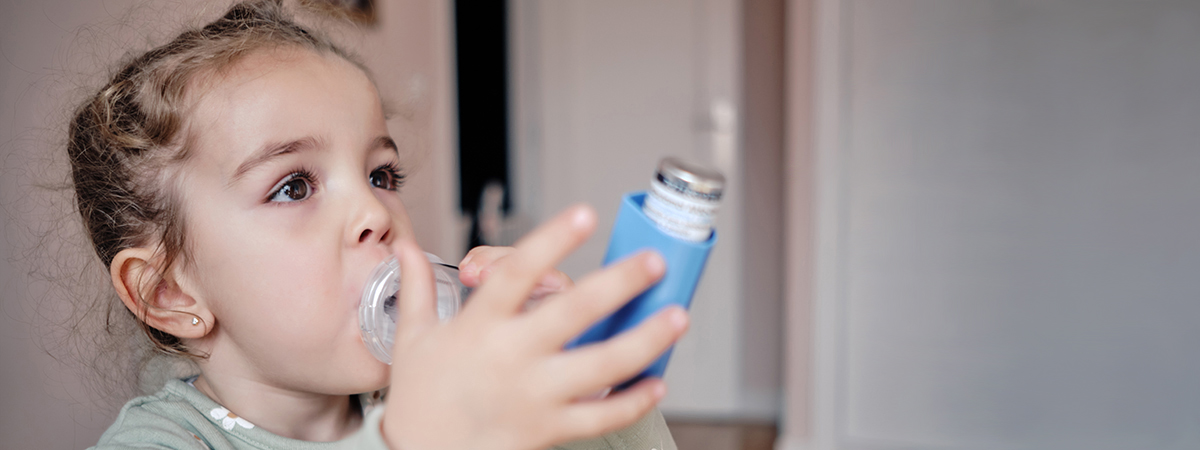 [Young child using inhaler with a spacer device.]