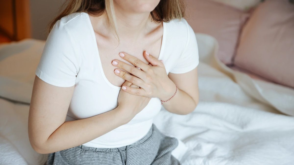 [Image of woman sitting on a bed holding her heart as if in pain.]