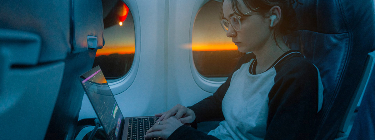 [Passenger on plane working on laptop at daybreak]