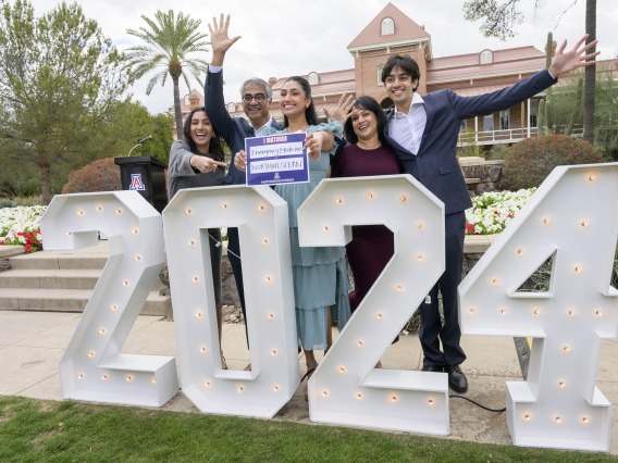 [A medical student and her family celebrate behind a large 2024 sign]