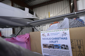 [Christmas donations in a box waiting in an airplane hanger to be loaded onto the waiting plane]