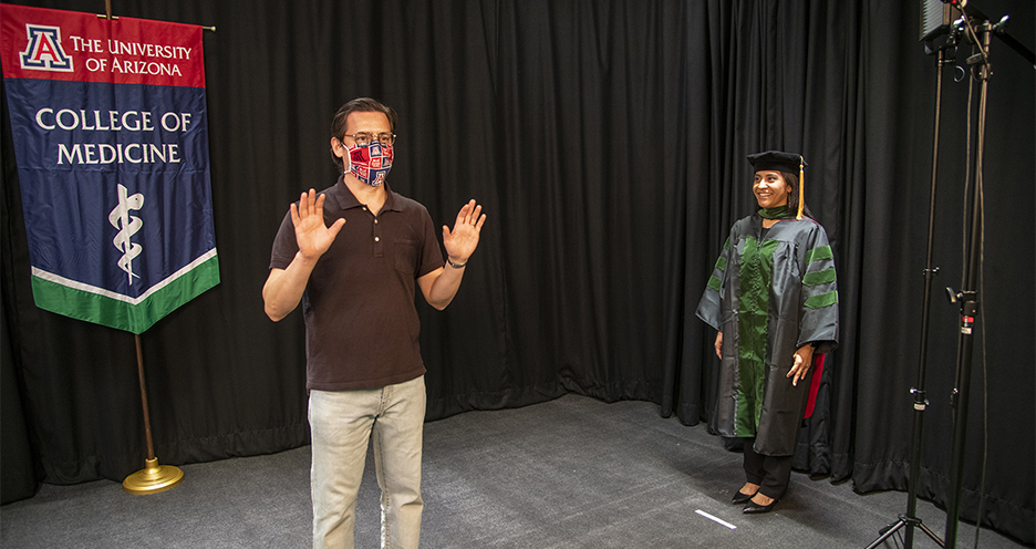 [Gilberto Vega shows medical student Cazandra Zaragoza how to simulate walking across a stage on graduation day. College of Medicine – Tucson student photos and videos will be used in the college’s virtual convocation event.]