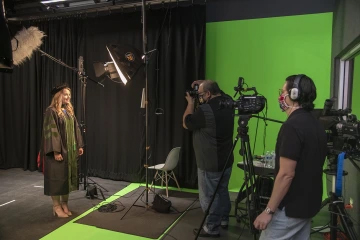 [Medical student Bethany Boczar wears her regalia for a studio shoot in the Health Sciences Innovation Building as Biocommunications photographer Mitchell Masilun and videographer Gilberto Vega film for the College of Medicine – Tucson’s virtual convocation ceremony.]