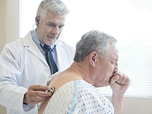 Older man coughing with doctor - Getty Images