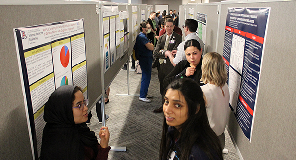 [Residents and faculty—including Drs. Anthony Witten (wearing mask) and Kevin Moynahan (center)—mingle during the judging portion of the poster contest during the 2024 Internal Medicine Research Academic Half Day for the Department of Medicine.]