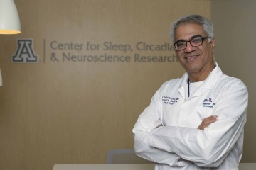 [Portrait of Sai Parthasarathy, MD, in lab coat in front of U of A Health Sciences Sleep, Circadian & Neuroscience Research sign]