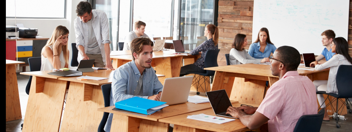 Employees in office talk together in different groups in open workspace setting.