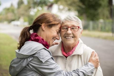 [Older woman with gray hair is hugged by younger woman while they're outside along walking pathway (Getty Images)]