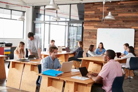 Employees in office talk together in different groups in open workspace setting.