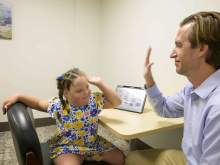 [Dan Combs, MD, assistant professor in pediatrics and sleep medicine at the University of Arizona College of Medicine – Tucson’s Department of Medicine, holds his hand up to a young Down syndrome patient for a high five in an office.]