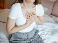 [Image of woman sitting on a bed holding her heart as if in pain]