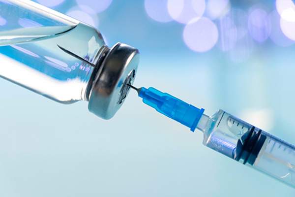 [Closeup photo of a needle being injected into a syringe with blue background.]