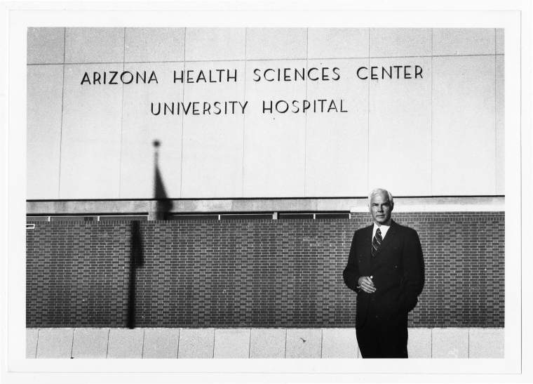 Pictured is a black and white photo of Dr. Merlin K. "Monte" DuVal, founding dean of the University of Arizona College of Medicine - Tucson in front of original signage for the then University Hospital of the Arizona Health Sciences Center