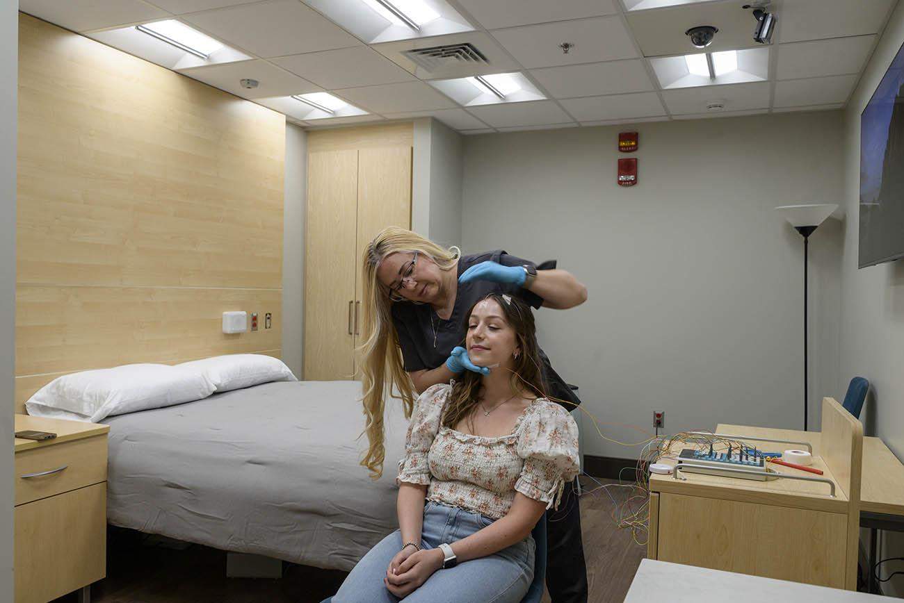 Sicily La Rue, lead sleep technologist at the Center for Sleep, Circadian and Neuroscience Research, applies polysomnographic electrodes, used for measuring sleep, to SCAN Lab technician Camryn Wellman in one of the sleep rooms.