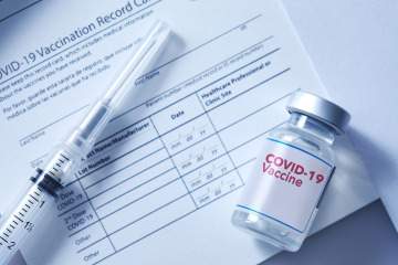 [Stock image of vaccine syringe and bottle on top of immunization paperwork.]