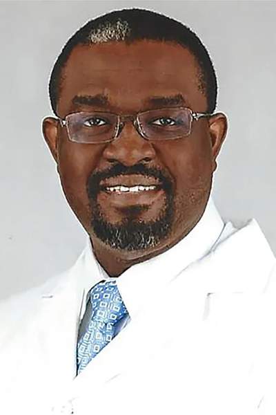 [Slightly graying black man with goatee and glasses wearing a physician's white coat and a white dress shirt with a blue tie]