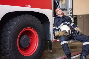 [A firefighter rests on a fire truck.]