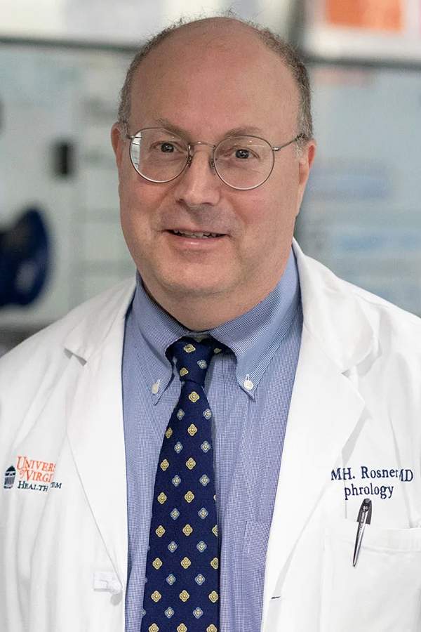 [Older balding white gentleman wearing glasses, a physicians white coat, blue dress shirt and tie in a clinic]
