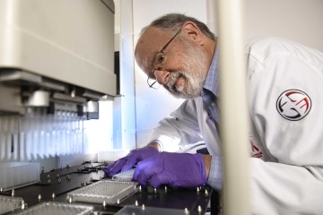 [John Galgiani in a lab coat and gloves working in a laboratory.]